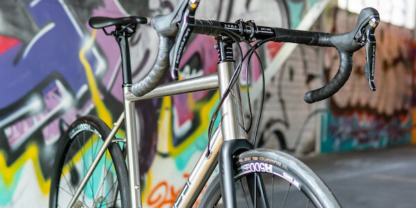 Bossi Summit titanium bicycle, viewed at an angle from the front, against a graffitied wall