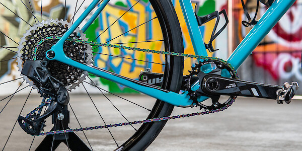 Drivetrain detail on a blue Open Cycles Wi.De gravel bike, a colourful graffitied wall in the background