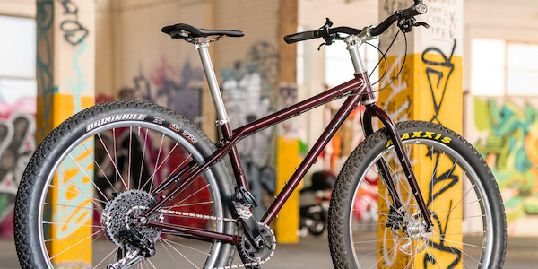 Surly Krampus mountain bike in Pickled Beet, viewed from the rear right side, in a colourful graffitied carpark