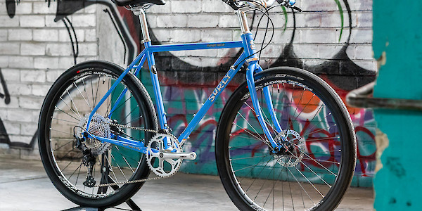 Surly Midnight Special bicycle in a custom build, Perry Winkle's Sparkle blue, viewed against a graffitied wall