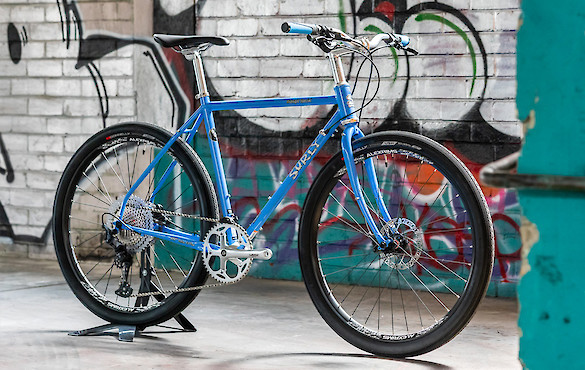 Surly Midnight Special bicycle in a custom build, Perry Winkle's Sparkle blue, viewed against a graffitied wall
