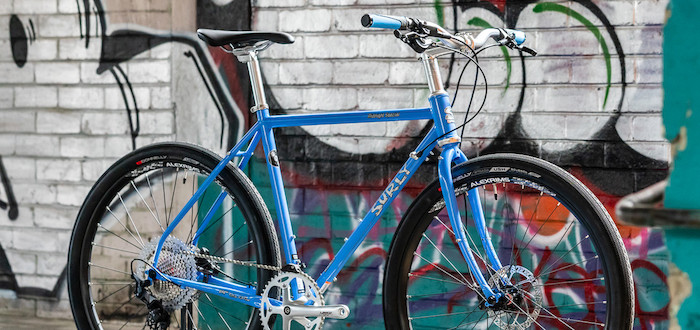 A custom-built Surly Midnight Special bicycle, Perry Winkle's Sparkle blue, viewed against a graffitied wall