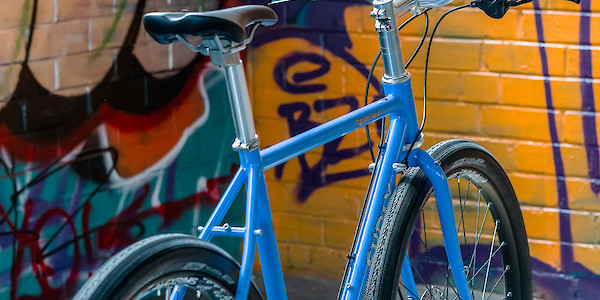 A custom-built Surly Midnight Special bicycle, Perry Winkle's Sparkle blue, viewed from the back and to the side, against a graffitied wall