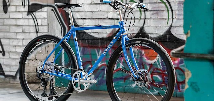 A custom-built Surly Midnight Special bicycle, Perry Winkle's Sparkle blue, viewed against a graffitied wall