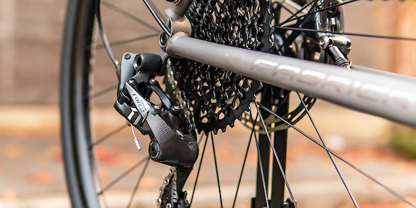 Cassette and rear derailleur detail on a custom titanium Bossi Grit bicycle, a stone wall in the background