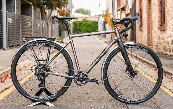 A titanium Bossi Grit gravel bicycle in a custom commuter build, shot in a quiet city alleyway