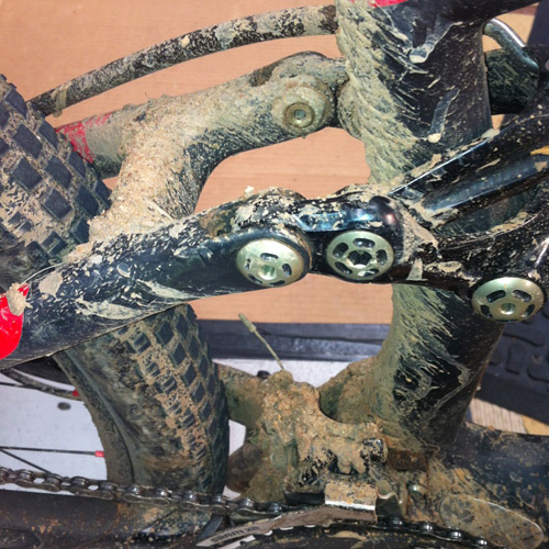Close-up detail of the rear triangle of a mountain bike frame covered in mud and grime