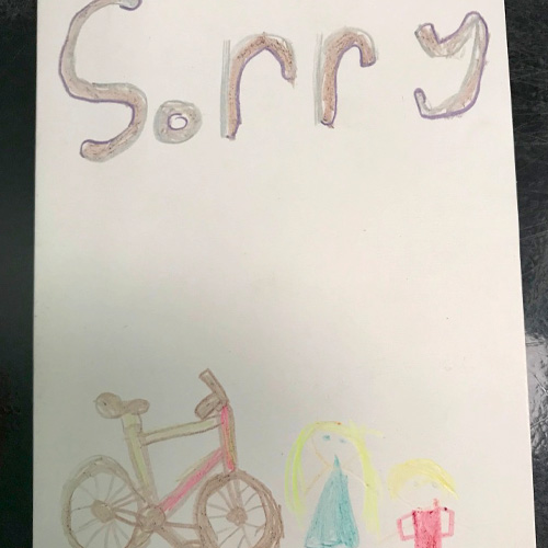A handmade card, written by a child, which says 'sorry' and shows an illustration of a bicycle and two children