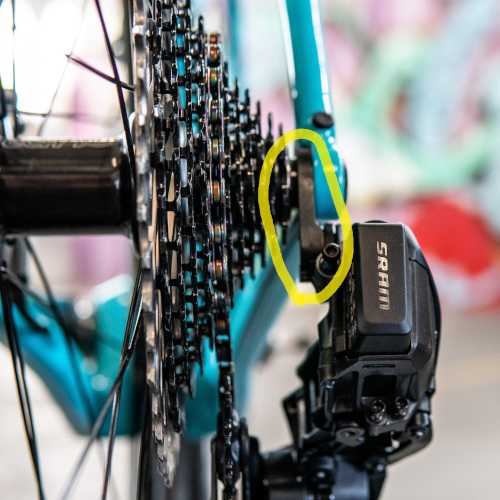 Close-up of a bicycle cassette (rear cogs) and derailleur from the rear, a yellow circle indicating the rear derailleur hanger