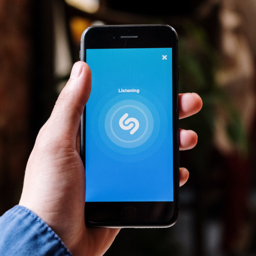 A hand holding a phone which is displaying the Shazam app