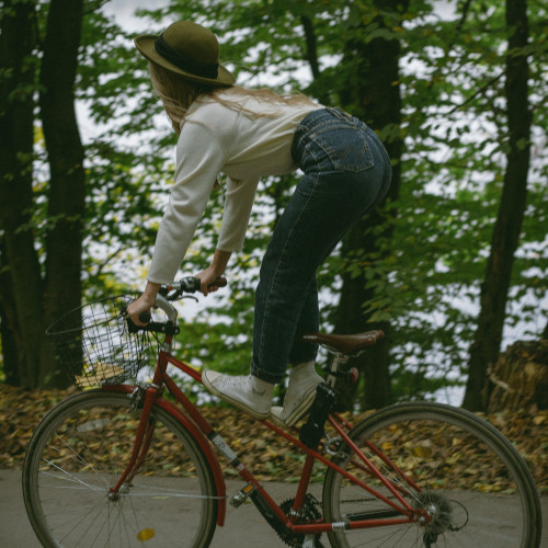 A young woman on a red bicycle, standing on the frame instead of sitting on the saddle