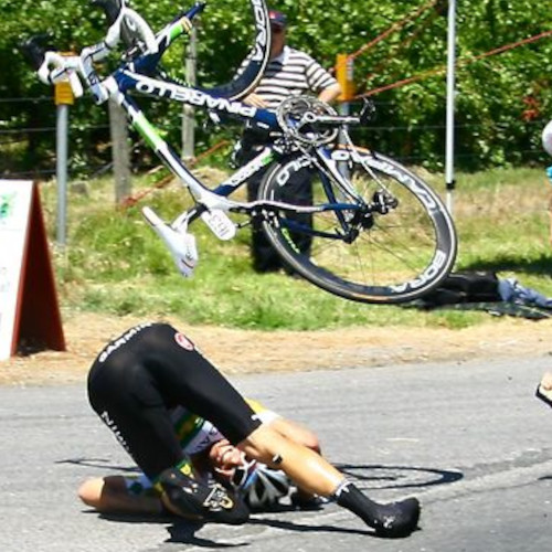 A cyclist hitting the road in a crash, his bicycle flying through the air above him