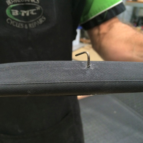 A mechanic at Bio-Mechanics Cycles & Repairs, holding a bicycle tube with a huge nail sticking out of it