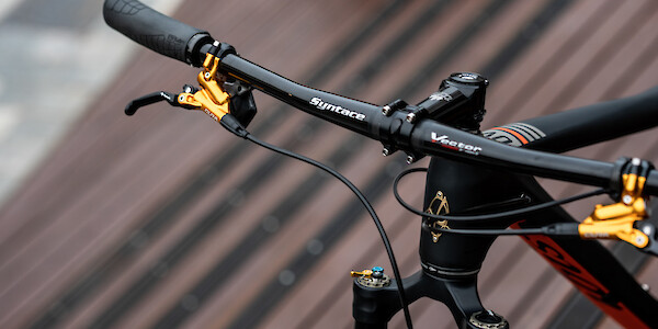Syntace carbon handlebars and gold Formula Cura brakes on an Ibis Cycles DV9 carbon mountain bike, wooden slats in the background