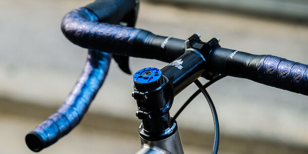 Close-up of Syntace carbon handlebars, a blue Tune top cap, and Ciclovation oil-slick handlebar tape on a titanium Bossi Summit bicycle