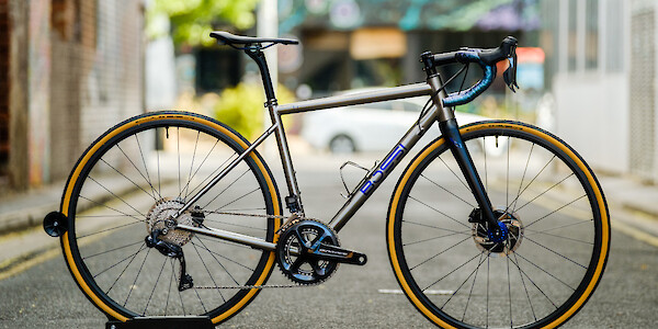 A custom-built titanium Bossi Summit drop-bar bicycle with blue highlights, shot in a city alleyway