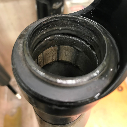 Close-up of a bicycle suspension fork during servicing, the seals and inside thick with grime
