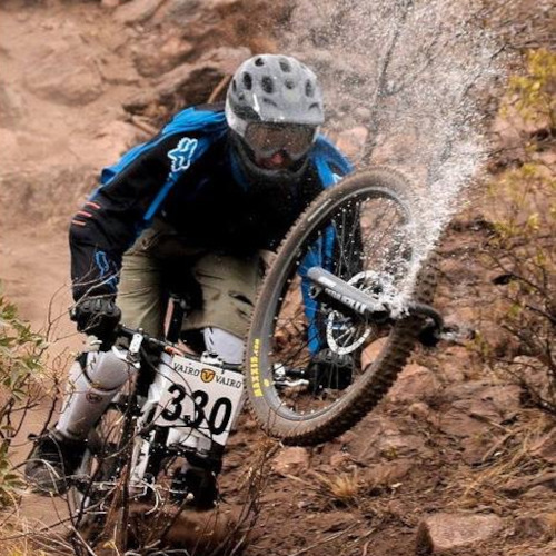 A mountain biker about to crash to the ground because his suspension forks have snapped off his bike, spraying liquid everywhere