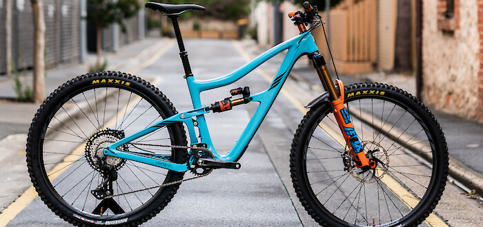 Ibis Ripmo V2 MTB in Bug Zapper Blue with custom orange touches, photographed in a rainy alleyway