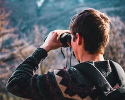 A young man with binoculars, looking out over a forest