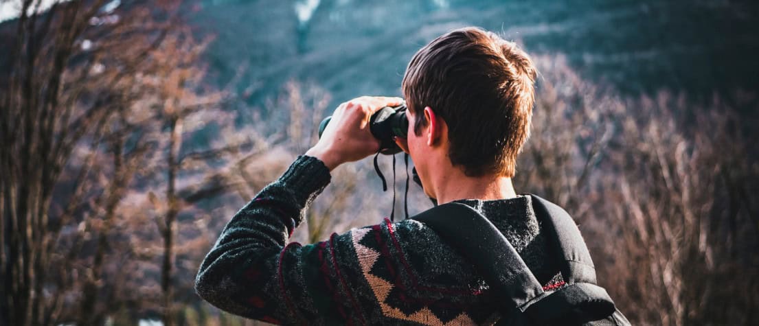 A young man with binoculars, looking out over a forest