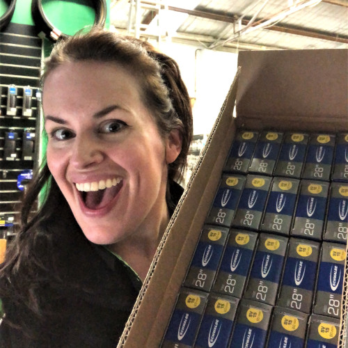 A woman with a big smile (Lia from Bio-Mechanics Cycles & Repairs) holding up a box of bicycle tubes
