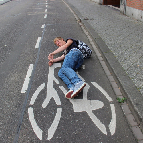 A young man lying on a road, pretending to ride the painted bicycle sign
