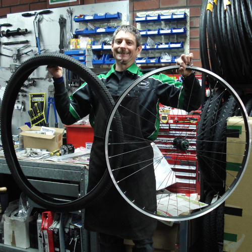 A bicycle mechanic holding up an enormous tyre and matching wheel