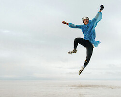 A young man wearing cycling gear and a rain jacket, jumping for joy on a deserted beach.