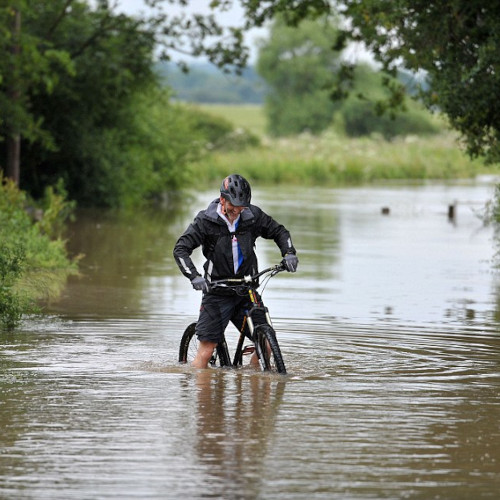 A cyclist trying to ride his bicycle through a river which is almost knee-deep