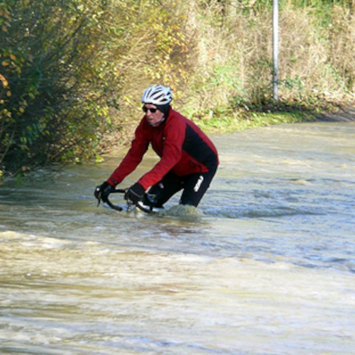A cyclist riding his bike through a river so high that all you can see of the bicycle are the handlebars