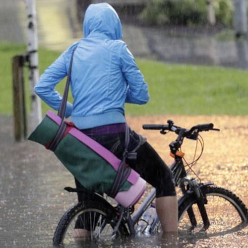 A cyclist toting a yoga mat, sitting on a bike amid a flooded street