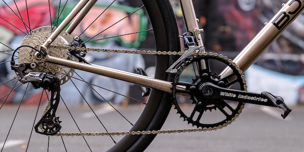 Detail of the gear components on a custom-built Bossi Summit road bike, including White Industries cranks. There's a wall covered in street art in the background.