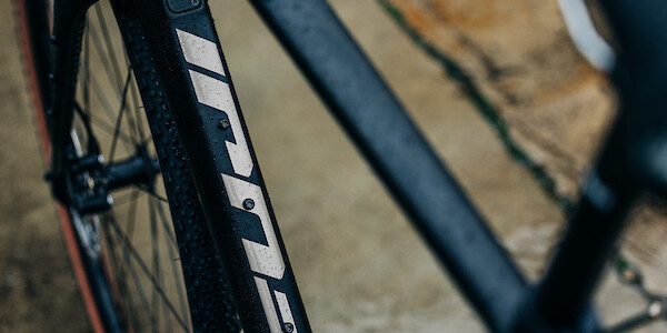 Close-up on the frame decal of a rain-drizzled Fuji Jari 1.3 Carbon, a wet concrete floor in the background