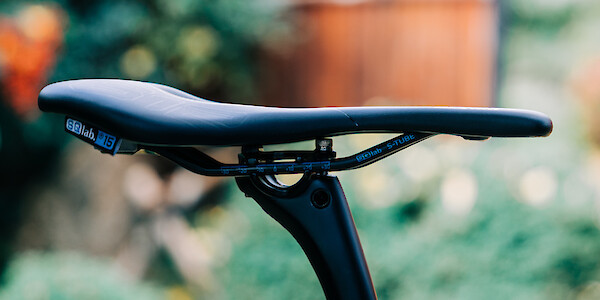 SQ-Lab bike saddle on a carbon seatpost, viewed from the side, with a garden in the background