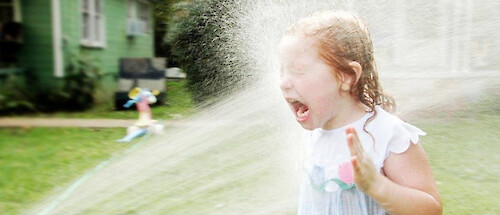 A little redheaded girl getting sprayed in the face by a hose. She's not enjoying it.