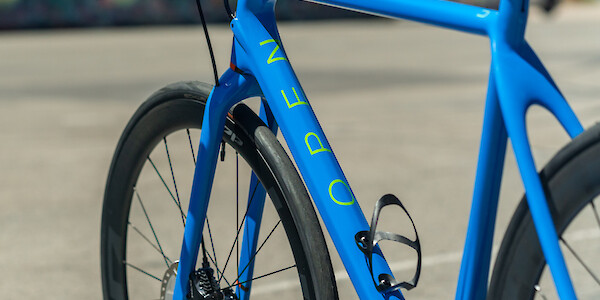 Frame decal detail on a custom-built Open Cycles U.P. carbon bicycle, including a Tune Wasserträger carbon bottle cage, asphalt in the background