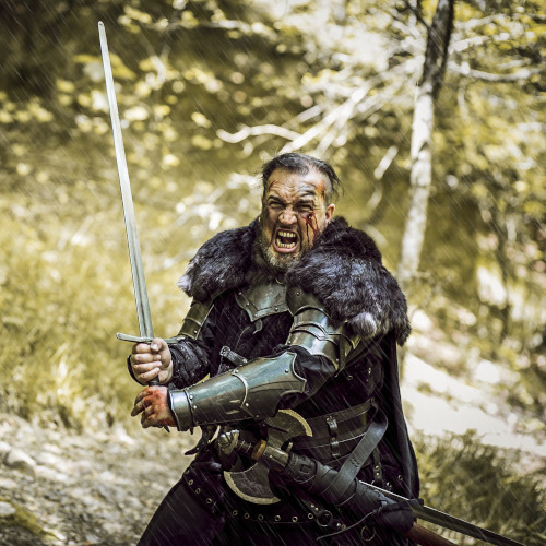 A heavily armoured mediaeval warrior, screaming and brandishing a sword, in a forest setting