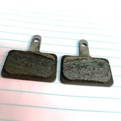 Close-up of a pair of bicycle disc brake pads with uneven grooves in them, indicating a problem with alignment