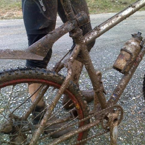 Partial view of a mountain bike caked in mud, the rider standing behind it