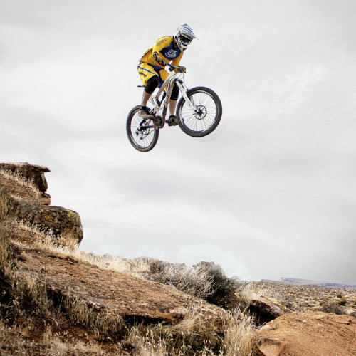 A mountain biker mid-air during a jump, in a dry and sandy environment