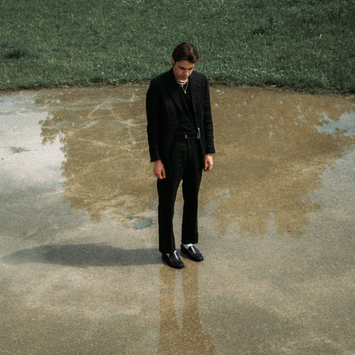 A depressed man standing on wet concrete, looking at the ground.