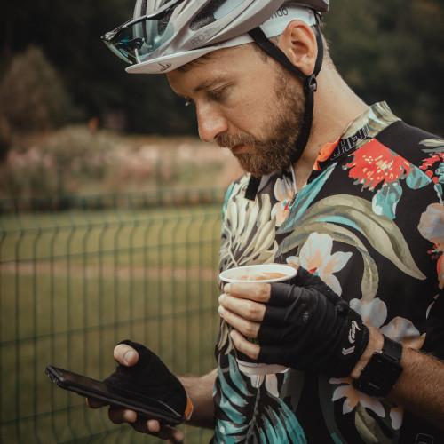 A bike rider holding a cup of coffee and looking down at his phone