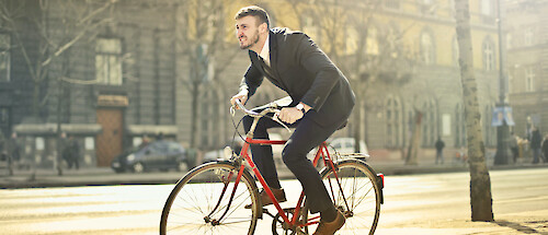A man riding a red bicycle in a city street, grimacing and looking uncomfortable