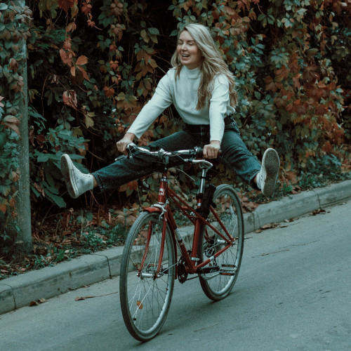 A young woman rolling along on a red bicycle, her legs straight out in front of her and her feet in the air