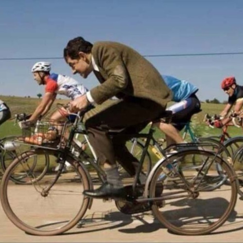 Mr Bean riding an old bicycle in a peloton of road cyclists, looking awkward