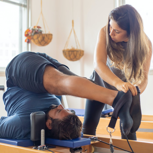 A therapist guiding her patient's legs over his head on a Pilates machine