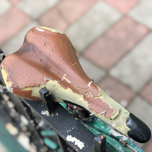 A peeling and damaged bicycle saddle, viewed from above, against an iron railing