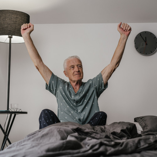 A mature gentleman sitting up in bed and giving a victory salute