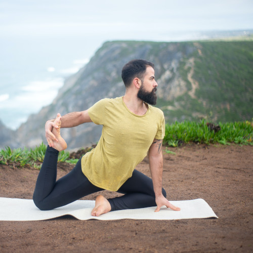 A bearded young man on a mat doing a yoga pose. (One-Legged King Pigeon Pose, to be exact.) There are mountains in the background.